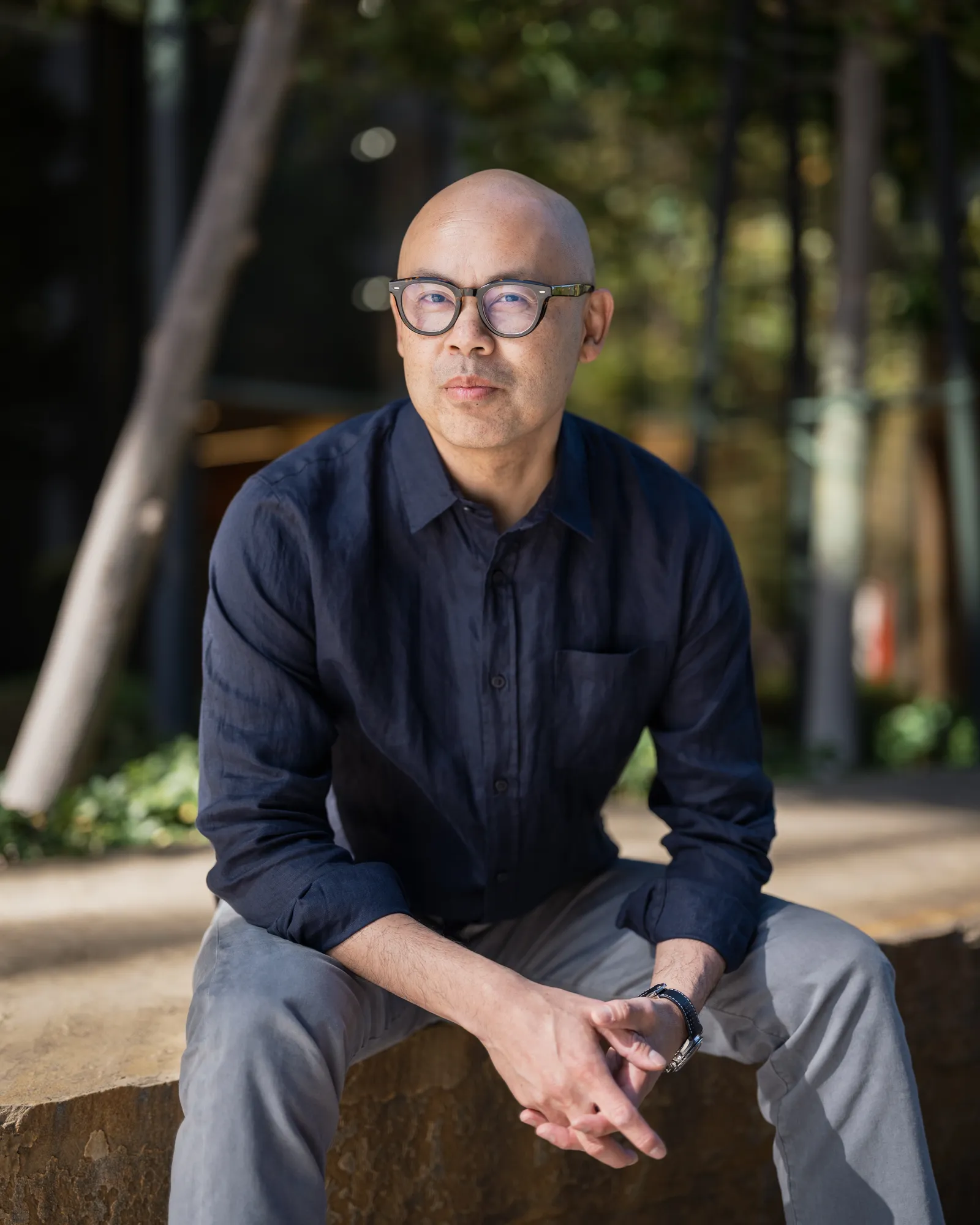 Environmental portrait of David Chan seated in front of glass and trees